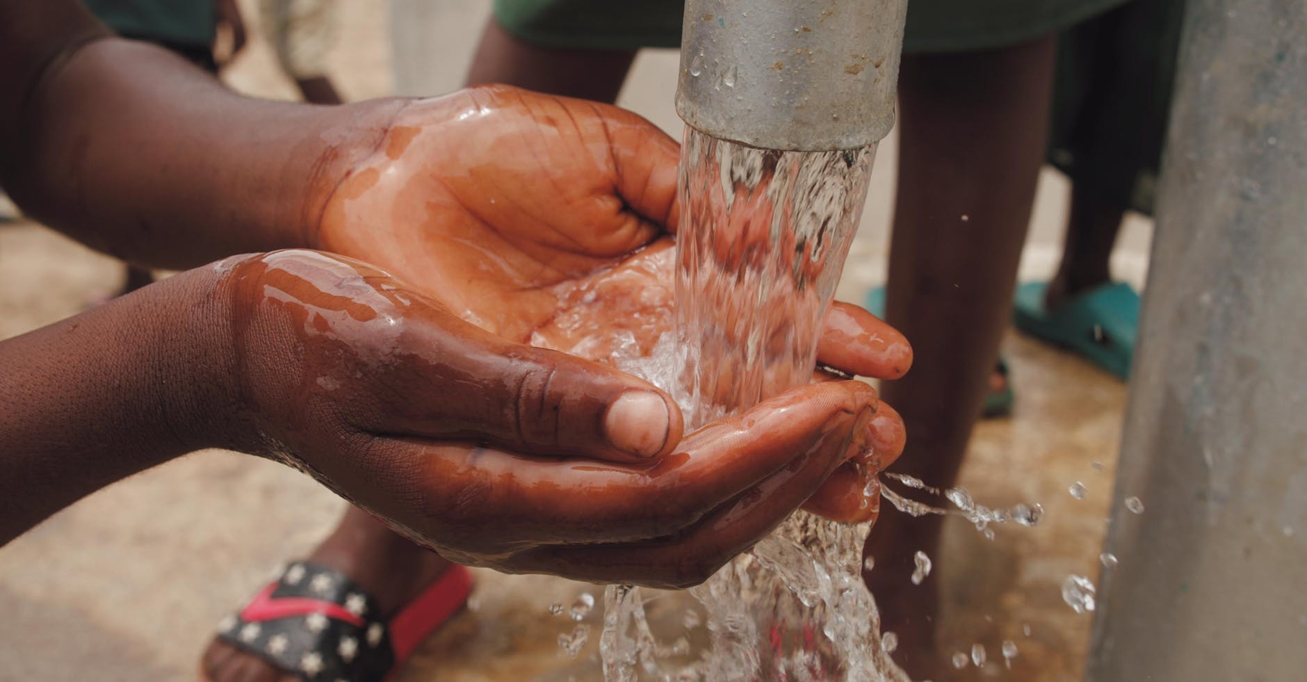 close up of a child s hands catching water from the spout of a water pump