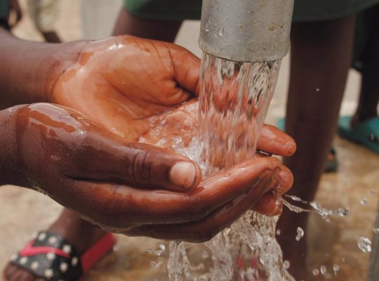 close up of a child s hands catching water from the spout of a water pump
